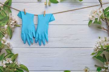 Rubber gloves, cleaning items on spring background, pastel wooden planks and spring blossoms. Close up. Spring regular cleaning. Flat lay. Empty place for text or logo.
