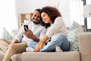 Fototapeta na wymiar technology, music and people concept - happy african american couple with smartphone and earphones at home