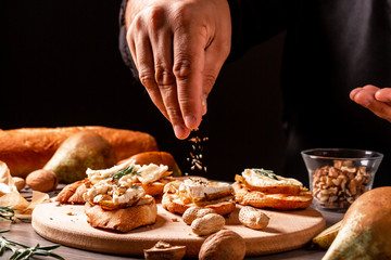 Appetizer bruschetta with pear, honey, walnut and brie camembert cheese cooking by chef hand. Appetizers table with italian antipasti snacks. space for text