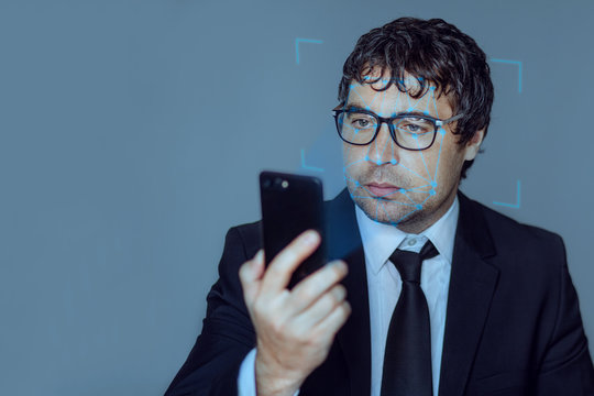 Face recognition. Biometric verification. Concept of a new facial recognition technology A young business man in a suit with a smartphone in his hands. Concept: dna system, science and technology.