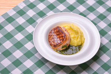 Filet mignon with mashed potatoes and pesto sauce served in a white plate over green plaid tablecloth. Beef steak.