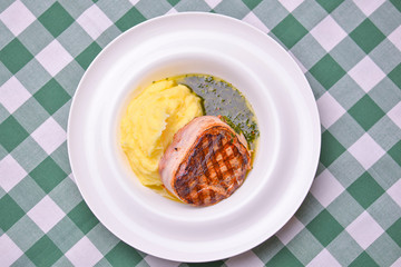 Filet mignon with mashed potatoes and pesto sauce served in a white plate over green plaid...