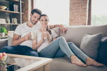Fototapeta premium Photo of domestic pretty charming lady handsome guy couple relaxing sit comfy couch stay home good mood quarantine hugging spend time together drink hot tea living room indoors