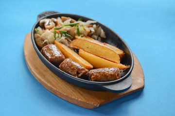 Grilled meat in mushroom's sauce and baked potato with cabbage mushroom salad in a pan over bright blue background.
