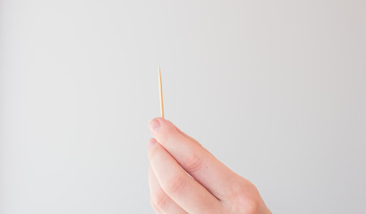Toothpick in female hand on white background. The concept of dental hygiene, oral health. Card with copy space for text