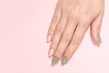 Fototapeta premium Closeup top view of beautiful two faded colors trendy manicure of green and pink nails with glossy silver stamp design isolated on pastel pink background. Winter or autumn style of nail design.