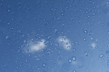 Regentropfen auf Fenster vor blauem Himmel mit Wolken