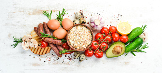 Ingredients of healthy nutrition. Cooking background: Eggs, oatmeal, sausages and fresh vegetables on a white wooden background.