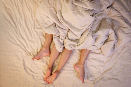 Close up of male and female feet on a bed  having sex under sheets in the bedroom.