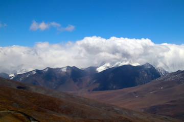 Obraz premium Plateau winding road, blue sky and white clouds, snowy mountains in the distance
