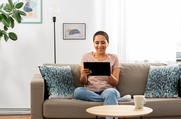 people, technology and leisure concept - happy young african american woman sitting on sofa with tablet pc computer at home