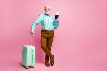 Full size photo of cool modern old grey hair man want go rest hold trolley documents wear teal turquoise shirt brown trousers suspenders footwear isolated pastel pink color background