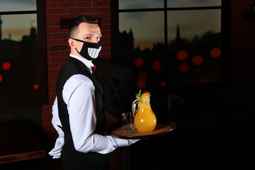 A waiter in a fun face mask holds a tray of lemonade in his hand. Restaurant customer service. The...