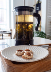 a white plate of almond cookies is placed on a wooden table. kettle French press in the background. close up