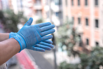 Fototapeta premium Male hands with blue gloves clapping outside the window during the quarantine for Covid 19 as a sign of appreciation for health personnel and law enforcement.