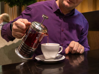Fototapeta na wymiar a man in a colored shirt pours tea into a Cup from a French press teapot.close up. copy space