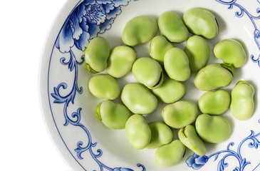 Close-up top view of fresh green broad beans on china plate isolated on white background. Healthy food. Macro.