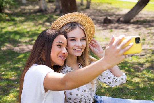 Two girlfriends of the blogger take selfies on the phone, the girls are photographed in the park