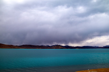 Obraz premium Plateau holy lake, blue-green lake water, coffee-colored distant mountains, rising water vapor and clouds