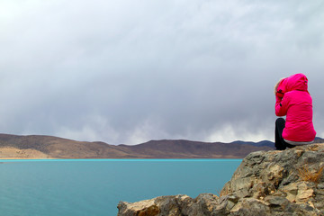 Fototapeta premium Plateau sacred lake, blue-green lake water, coffee-colored distant mountains, back view of beautiful women in red clothes by the lake