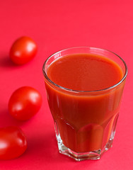 A glass of tomato juice and a few pieces of cherry next to the red background, monochrome shot