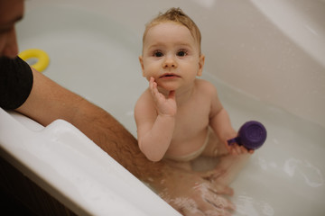 A cute baby girl bathes in a bath with toys and look to the camera