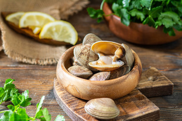 Raw clams in a wooden bowl on a brown wooden table. Seashell