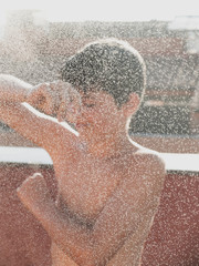 Cheerful young male enjoying a shower by hose outdoors in the terrace