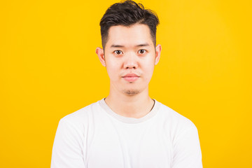 Close up portrait happy Asian handsome young man smiling standing wearing white t-shirt looking to camera, studio shot isolated yellow background