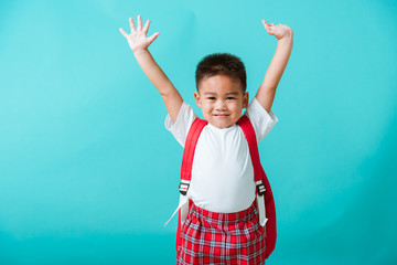 Back to school. Portrait happy Asian cute little child boy in uniform smile raise hands up glad when go back to school, isolated blue background. Kid from preschool kindergarten with school backpack - obrazy, fototapety, plakaty
