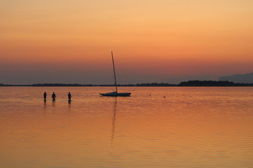 sailing boat moored on the sea at sunset and headland on the background