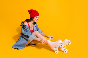 Full size profile side photo of positive youth millennial girl sit floor tie laces roller skates wear red headwear singlet jeans shorts isolated over bright color background © deagreez