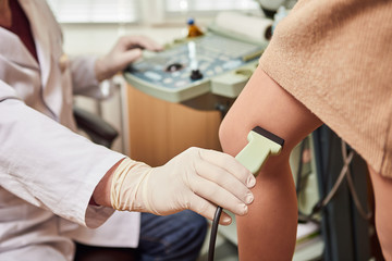 Obraz premium Lekarz w białym mundurze z wyposażeniem diagnostycznym wykonuje badanie USG żył nóg pacjentki. Flebolog pracujący w nowoczesnej klinice z chorobą żylaków