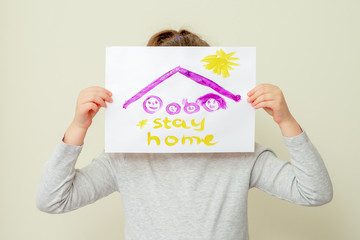 Child is holding a picture of family silhouette under the roof and words Stay Home covering her face on yellow background. Stay Home concept.