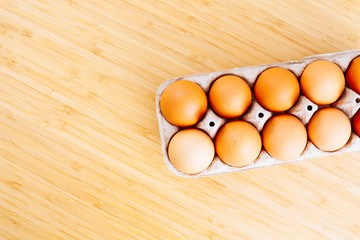 Overhead view of fresh brown chicken eggs in open egg carton box on wooden table background. Top view with copy space.