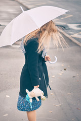 woman stands under an umbrella in a reflection of puddles. girl holding a stuffed toy