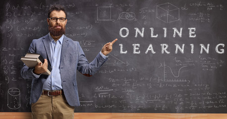 Male teacher holding books and pointing at a blackboard with text online learning