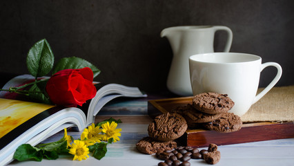 Obraz na płótnie Canvas Coffee cups and chocolate chip baked cookies with red roses on books on a wooden table