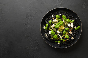 Black pasta spaghetti squid Ink with sauce Pesto in black bowl on black stone background. Top view.