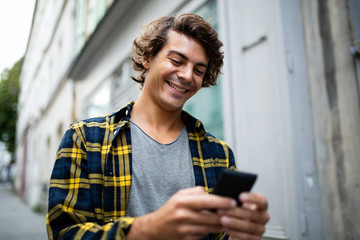 happy young guy walking in city looking at mobile phone