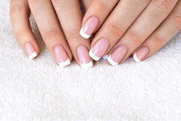 Female fingers with beautiful French manicure on white terry towel, close up, selective focus.
