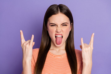 Closeup photo of attractive crazy funky lady long brown straight hairstyle show finger horns sticking tongue wear casual orange striped t-shirt isolated pastel purple color background