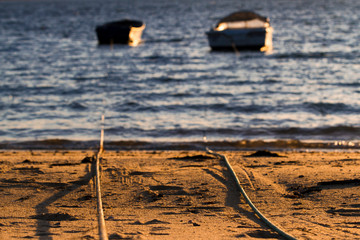 Cuerdas de pesca en una playa que atan dos barcas de pescadores con una puesta de sol
