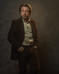 Fashionable middle aged man in dark brown suit in front of grey wall. Low key studio shot.