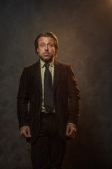 Cool middle aged businessman in dark brown suit and black tie in front of grey wall. Low key studio shot.