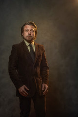 Cool middle aged businessman in dark brown suit and black tie in front of grey wall. Low key studio shot.