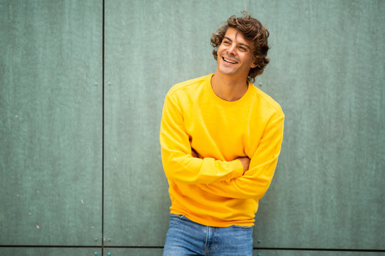 male fashion model in yellow sweater laughing by green background