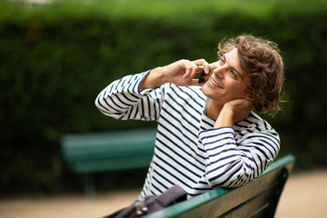 handsome young man sitting on park bench talking with cellphone