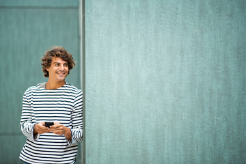 cool young man smiling with mobile phone by green background
