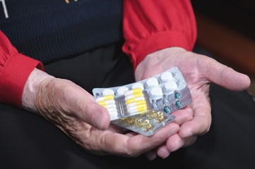 Closeup hands of an old woman hold many different pills in hands. The concept of drug selection and the health of the older generation